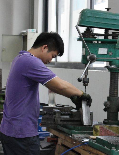 Engineer operating a drill press while fabricating a machine part